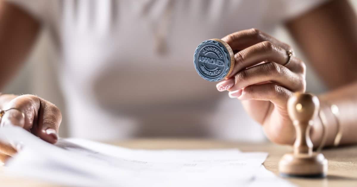 Person holding a stamp and signing legal documents for property settlement.